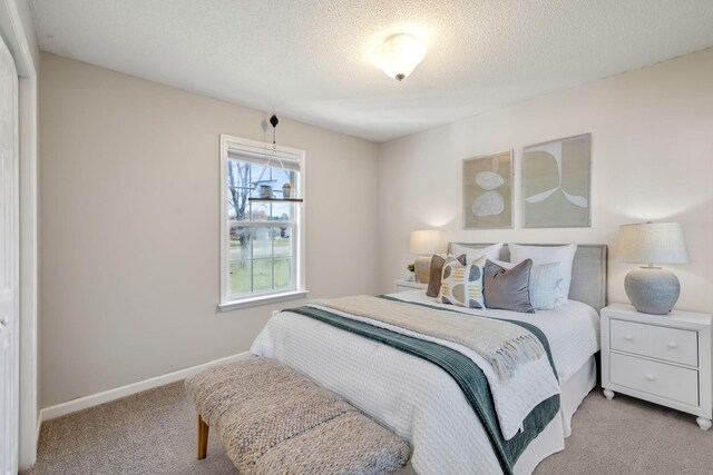 bedroom featuring light colored carpet, a textured ceiling, and baseboards
