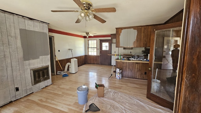 kitchen with light wood-type flooring, heating unit, wooden walls, light countertops, and ceiling fan