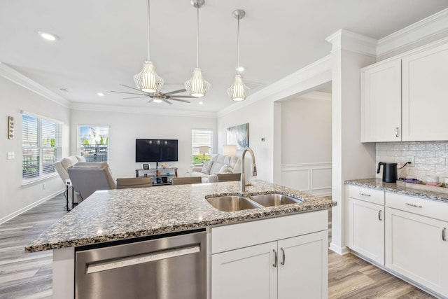 kitchen featuring ornamental molding, a center island with sink, a sink, stainless steel dishwasher, and stone counters