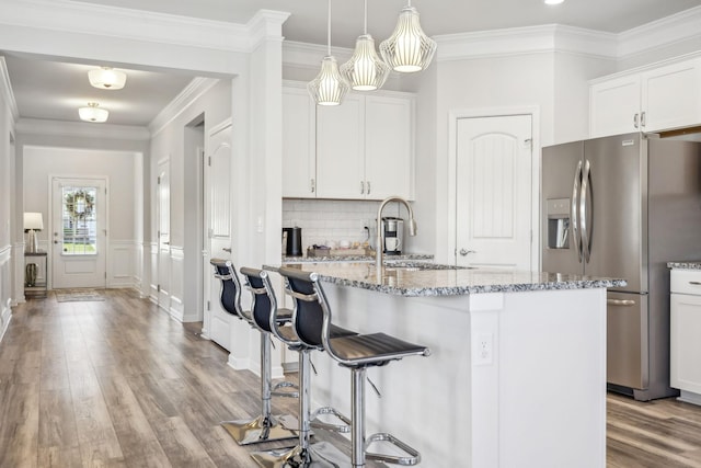 kitchen featuring light stone countertops, stainless steel fridge with ice dispenser, a kitchen bar, wood finished floors, and white cabinets