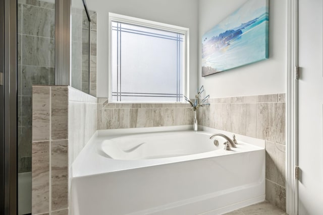 bathroom with a tile shower, tile walls, and a garden tub