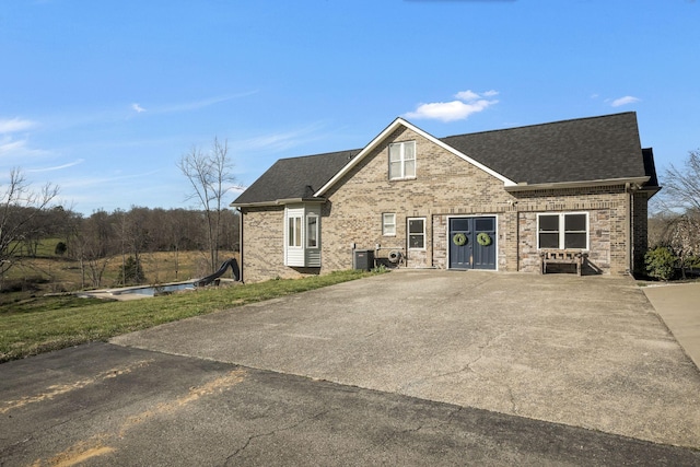 view of front of home with central air condition unit, brick siding, and roof with shingles