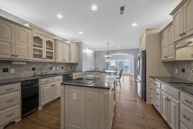 kitchen with black electric stovetop, arched walkways, freestanding refrigerator, and a sink