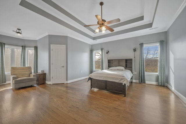bedroom featuring baseboards, a raised ceiling, wood finished floors, and ornamental molding