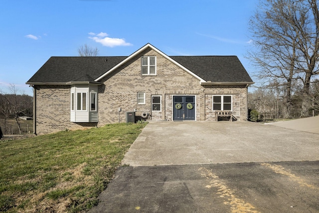 view of front of property featuring a front lawn, brick siding, central AC, and a shingled roof