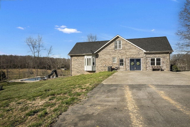 view of front of property with brick siding, central AC, a front yard, and roof with shingles