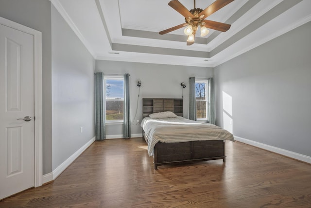 bedroom with a tray ceiling, crown molding, wood finished floors, and baseboards