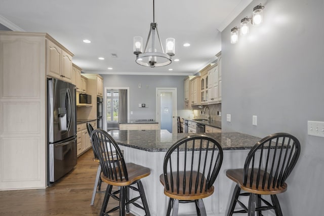 kitchen with a kitchen island, crown molding, appliances with stainless steel finishes, a peninsula, and a notable chandelier