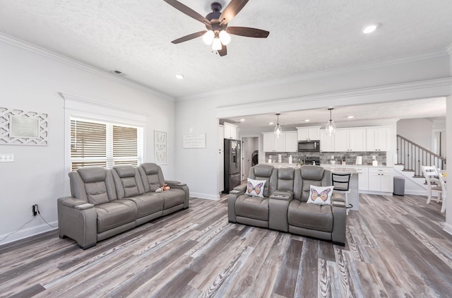 living area with stairway, crown molding, a ceiling fan, and wood finished floors