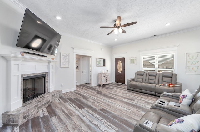 living room with a ceiling fan, a textured ceiling, wood finished floors, a fireplace, and crown molding