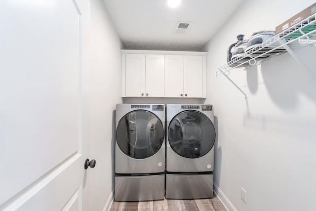 laundry room featuring visible vents, wood finished floors, cabinet space, baseboards, and washing machine and clothes dryer