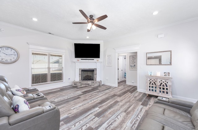 living area with a fireplace with raised hearth, wood finished floors, crown molding, baseboards, and ceiling fan