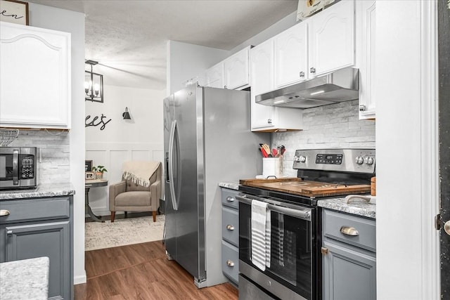 kitchen with gray cabinetry, under cabinet range hood, stainless steel appliances, dark wood-style floors, and white cabinetry