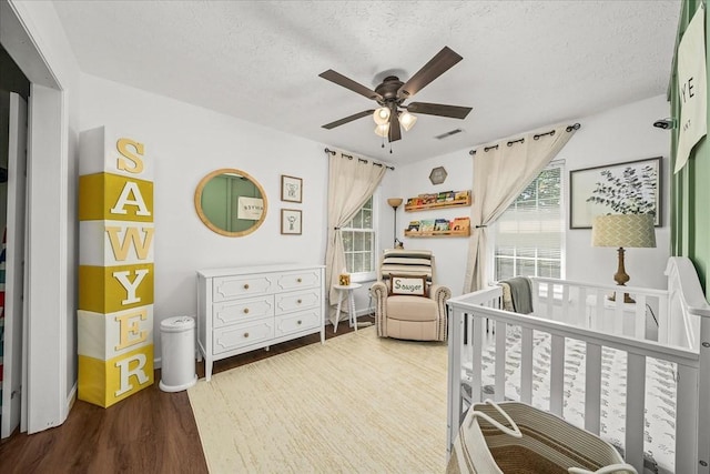 bedroom featuring multiple windows, a nursery area, wood finished floors, and a textured ceiling