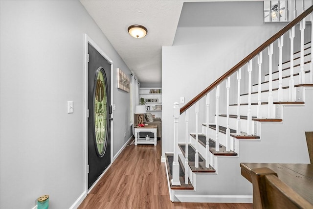 foyer entrance with stairs, baseboards, and wood finished floors