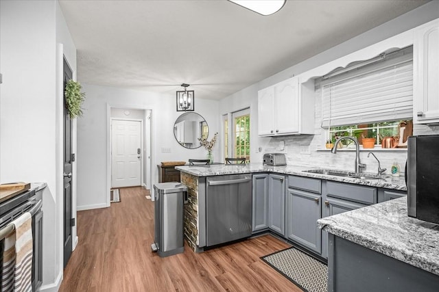 kitchen with decorative backsplash, stainless steel dishwasher, wood finished floors, white cabinetry, and a sink