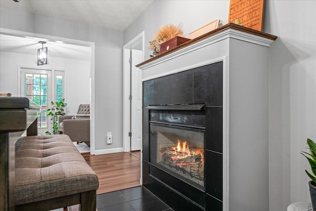 living area with a glass covered fireplace, dark tile patterned floors, baseboards, and a textured ceiling