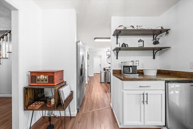 kitchen with dark countertops, white cabinets, refrigerator, and light wood-style floors