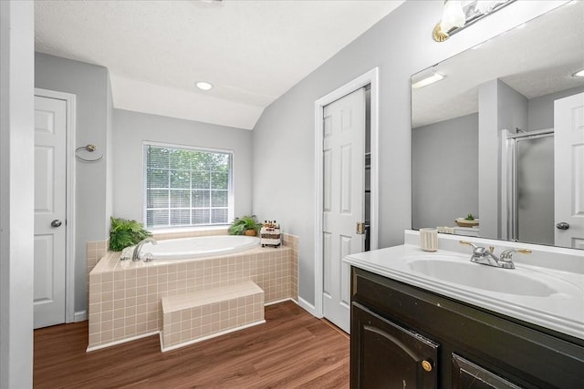 full bath featuring vanity, wood finished floors, a stall shower, vaulted ceiling, and a garden tub