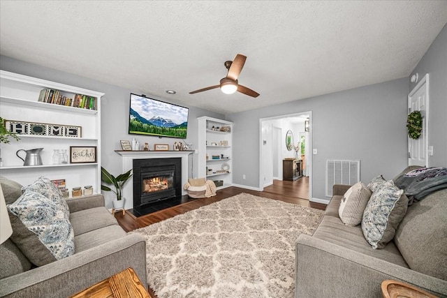 living room featuring visible vents, wood finished floors, ceiling fan, and a fireplace with flush hearth