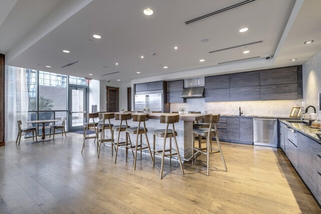 kitchen with light wood finished floors, wall chimney range hood, appliances with stainless steel finishes, modern cabinets, and a sink