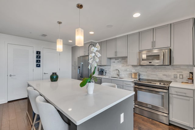kitchen featuring gray cabinets, a sink, tasteful backsplash, a kitchen island, and stainless steel appliances