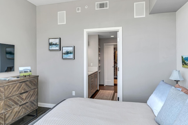 bedroom with visible vents, a walk in closet, baseboards, and dark wood-style flooring