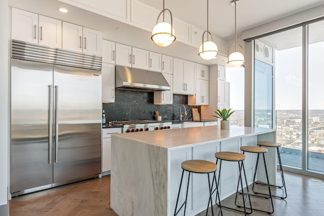 1616 W End Ave Unit 2602, Nashville, TN 37203 - kitchen with a kitchen bar, under cabinet range hood, tasteful backsplash, white cabinetry, and stainless steel appliances