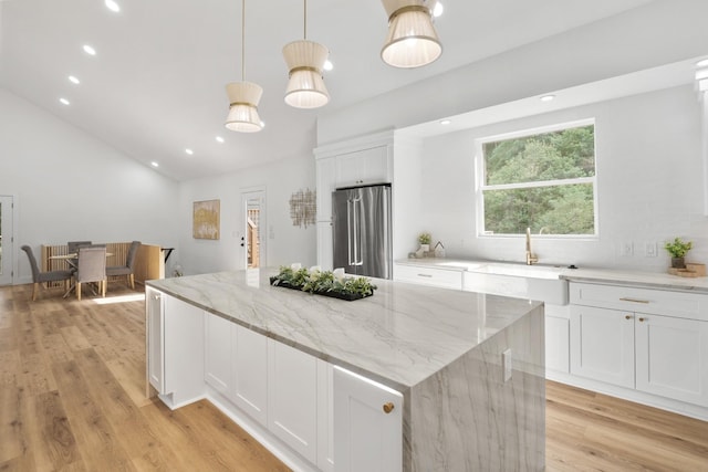 kitchen featuring light wood finished floors, a kitchen island, light stone countertops, high quality fridge, and white cabinets