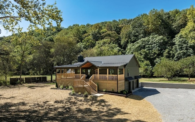 view of front of home with a standing seam roof, a forest view, driveway, and metal roof