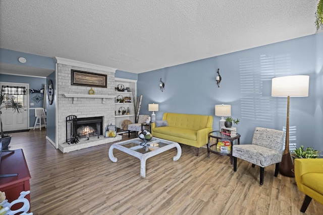 living area with a brick fireplace, a textured ceiling, and wood finished floors