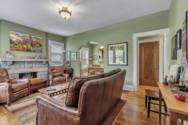 living room featuring arched walkways, hardwood / wood-style floors, a fireplace, and a textured wall