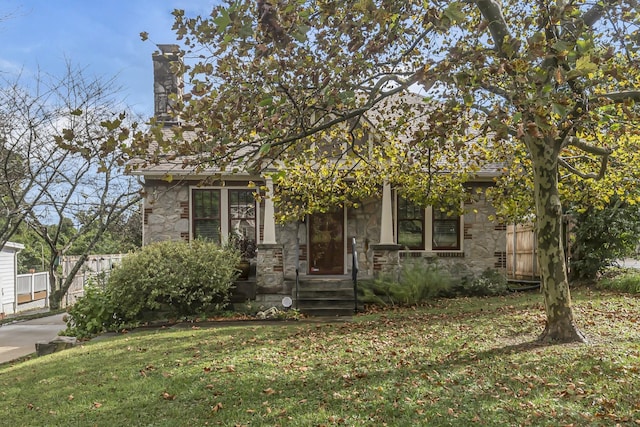 view of front of house with a front yard, fence, stone siding, and a chimney