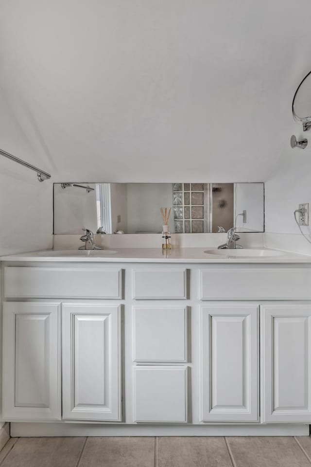 full bath featuring tile patterned floors, a sink, vaulted ceiling, and double vanity