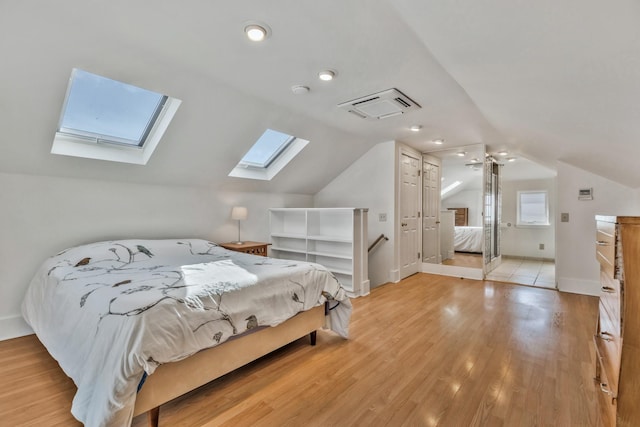 bedroom featuring baseboards, visible vents, light wood finished floors, vaulted ceiling with skylight, and a closet