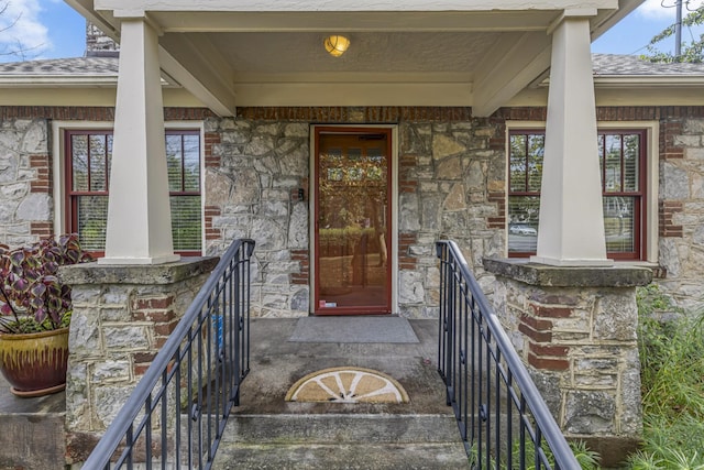 property entrance with a porch, stone siding, and a shingled roof