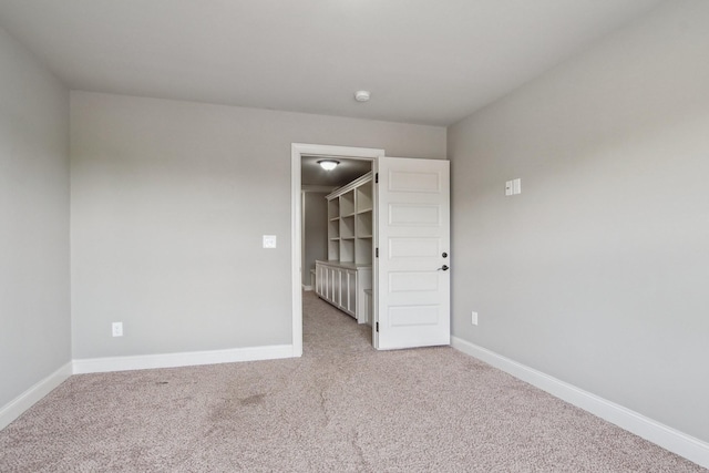 unfurnished bedroom with a walk in closet, carpet floors, and baseboards