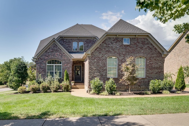 french country style house with brick siding, a front yard, and a shingled roof