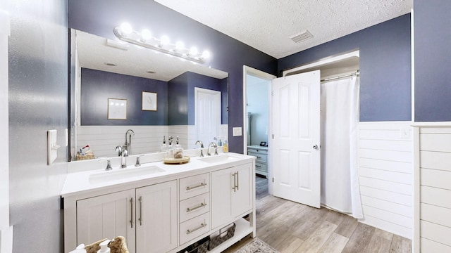 bathroom featuring visible vents, a textured ceiling, a wainscoted wall, and a sink