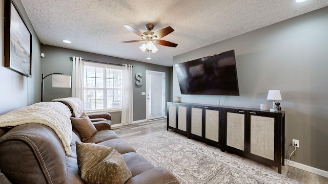 living area with a textured ceiling, baseboards, ceiling fan, and wood finished floors