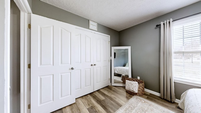 bedroom with a closet, baseboards, a textured ceiling, and wood finished floors
