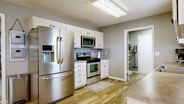 kitchen with backsplash, light wood-style floors, appliances with stainless steel finishes, and white cabinetry