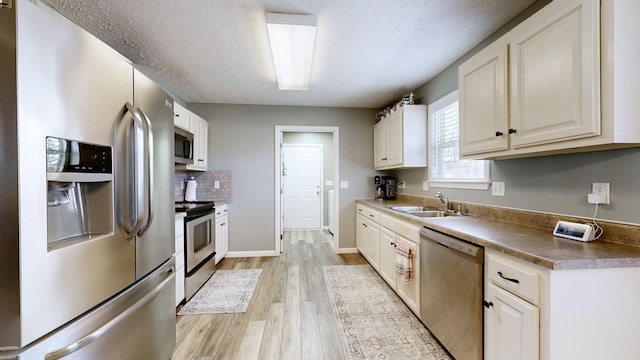 kitchen with a sink, backsplash, a textured ceiling, light wood-style floors, and appliances with stainless steel finishes