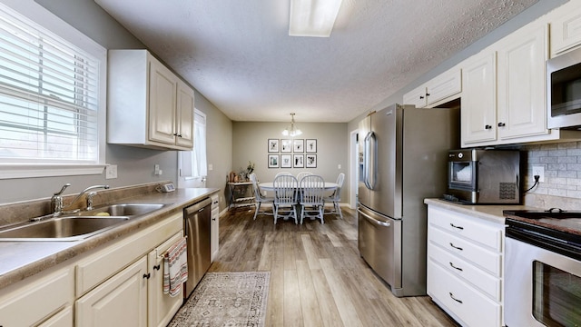 kitchen with light wood-type flooring, a sink, stainless steel appliances, an inviting chandelier, and decorative backsplash