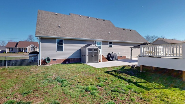 rear view of property featuring fence, a lawn, a patio area, a storage unit, and an outbuilding