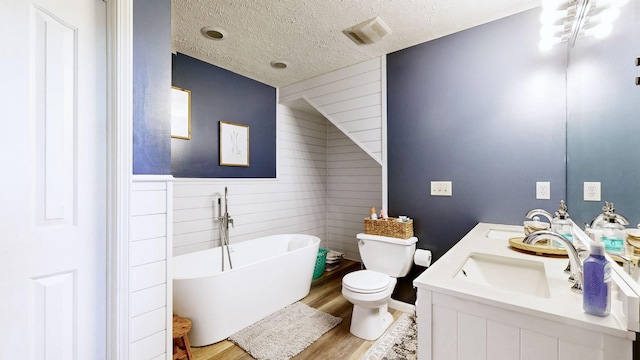 bathroom featuring wood finished floors, a freestanding tub, wood walls, a textured ceiling, and toilet