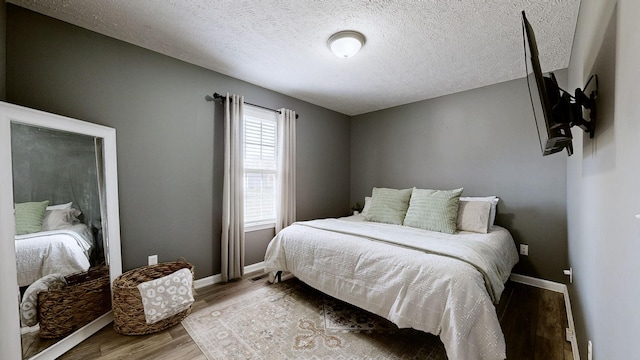 bedroom featuring wood finished floors, baseboards, and a textured ceiling