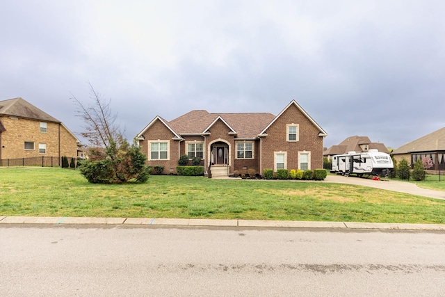 view of front of property featuring a front yard, fence, brick siding, and concrete driveway