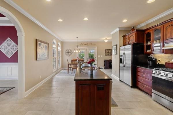 kitchen with stainless steel appliances, a kitchen island with sink, dark countertops, and ornamental molding