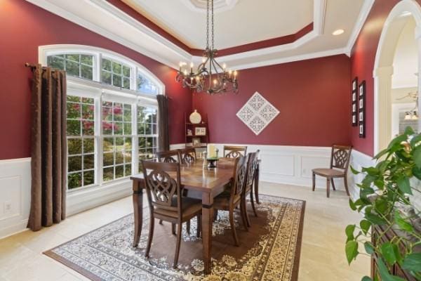 dining space with a decorative wall, crown molding, wainscoting, arched walkways, and a tray ceiling